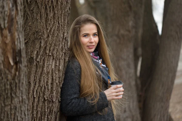 Retrato de una hermosa chica con una bebida caliente a principios de primavera al aire libre . — Foto de Stock