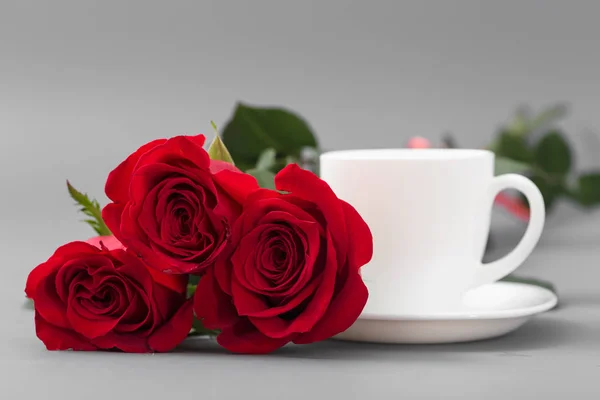 Κόκκινα τριαντάφυλλα με ένα φλιτζάνι καφέ άσπρο χρώμα σε γκρι φόντο — Φωτογραφία Αρχείου