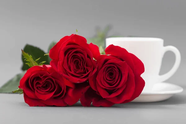 Red roses with a coffee cup of white color on a gray background — Stock Photo, Image