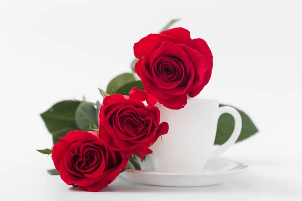 Rosas vermelhas com xícara de café de cor branca em um fundo branco . — Fotografia de Stock