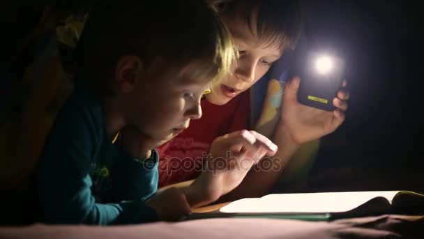 I bambini leggono un libro sotto una coperta con una torcia elettrica — Video Stock