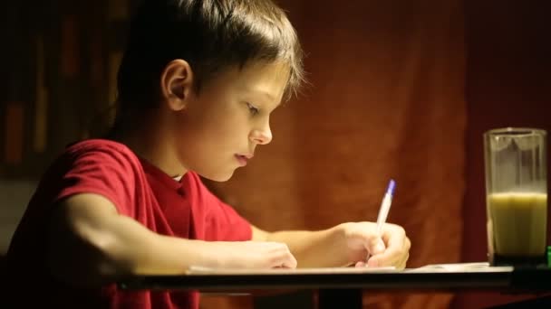 Мальчик за столом пишет в блокноте — стоковое видео