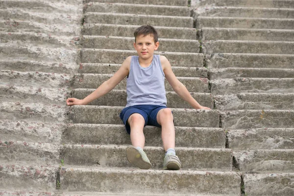 Un adolescente con una maglietta si siede su gradini di cemento — Foto Stock