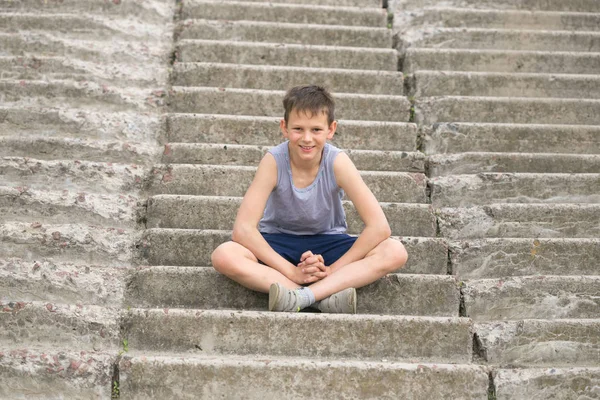 Подросток в футболке сидит на бетонных ступеньках — стоковое фото