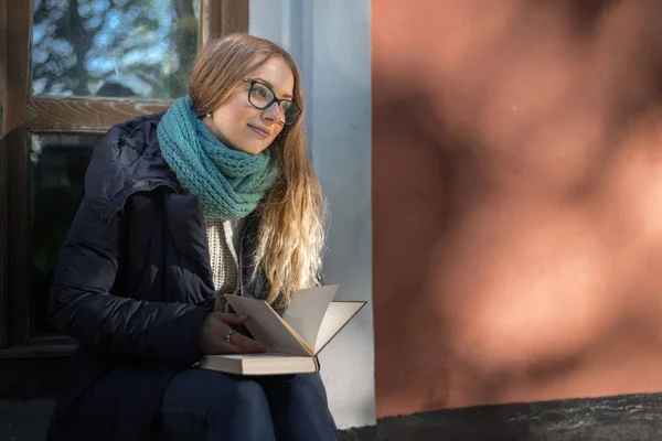 The girl is reading a book sitting by the window — Stock Photo, Image