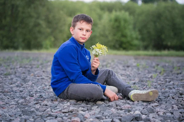 Ragazzo adolescente seduto su ghiaia con bouquet . — Foto Stock