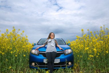 Güzel kız sarı bir alan üzerindeki arabanın yanında duruyor