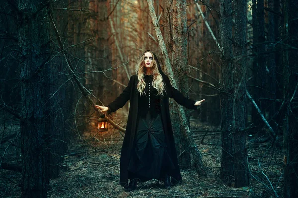 Halloween. bella ragazza con una lanterna in un vestito nero nella foresta . — Foto Stock