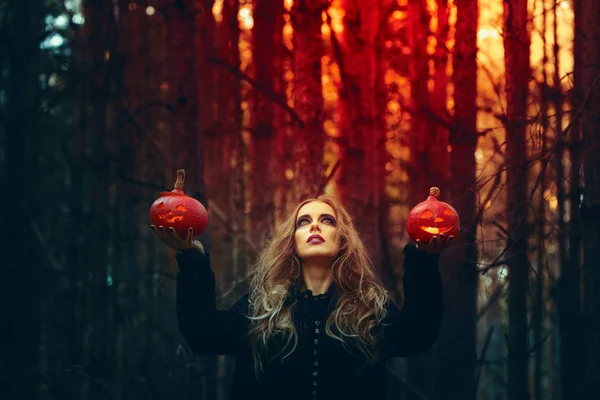 Halloween. belle fille avec une citrouille dans une robe noire dans la forêt . — Photo