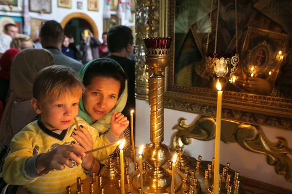 Een kind met zijn moeder verlichting een kaars in een kerk. — Stockfoto