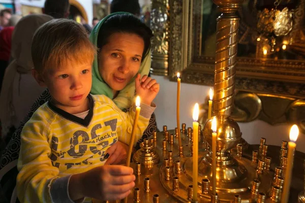 Een kind met zijn moeder verlichting een kaars in een kerk. — Stockfoto