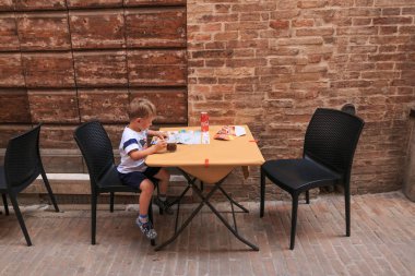 Urbino, İtalya - 9 Ağustos 2017: çocuk bir İtalya sokakta bir kafeterya masada oturuyor.