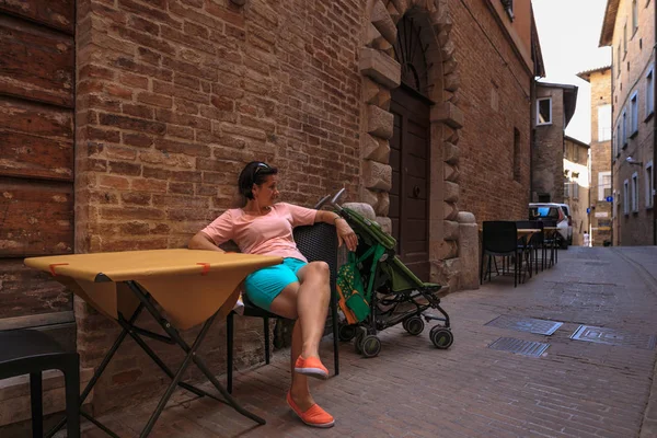 La mujer está sentada en una mesa en la estrecha calle de Italia . — Foto de Stock