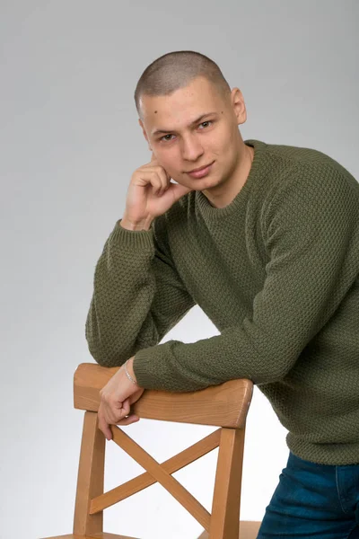 A young man is skinhead in a green military style sweater. studio. — Stock Photo, Image
