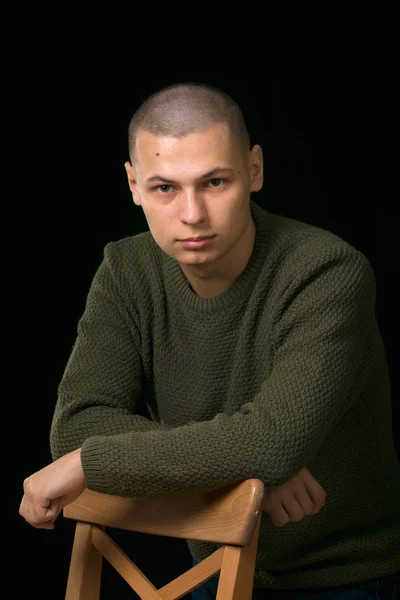Ένας νεαρός άνδρας είναι σκίνχεντ σε ένα πουλόβερ πράσινο στρατιωτικό στυλ. στούντιο. — Φωτογραφία Αρχείου