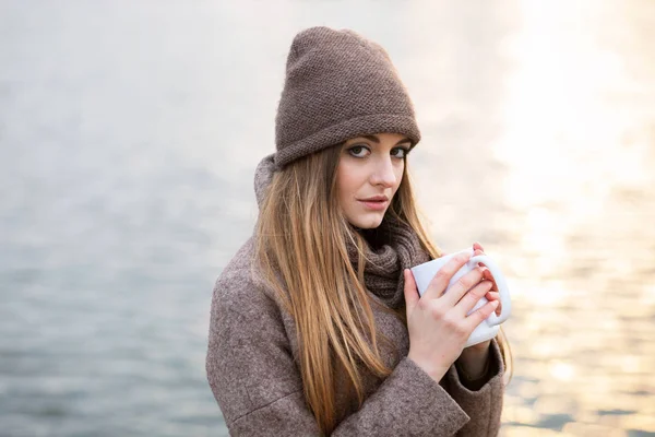 Menina em um chapéu de malha e cachecol com uma caneca na queda na natureza — Fotografia de Stock