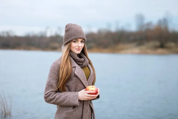 Mädchen mit Strickmütze und Schal mit einem Apfel im Herbst auf die Natur. — Stockfoto