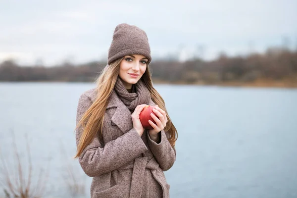 Chica en una gorra de punto y bufanda con una manzana en el otoño en la naturaleza . — Foto de Stock