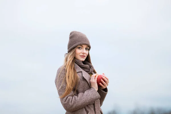 Mädchen mit Strickmütze und Schal mit einem Apfel im Herbst auf die Natur. — Stockfoto