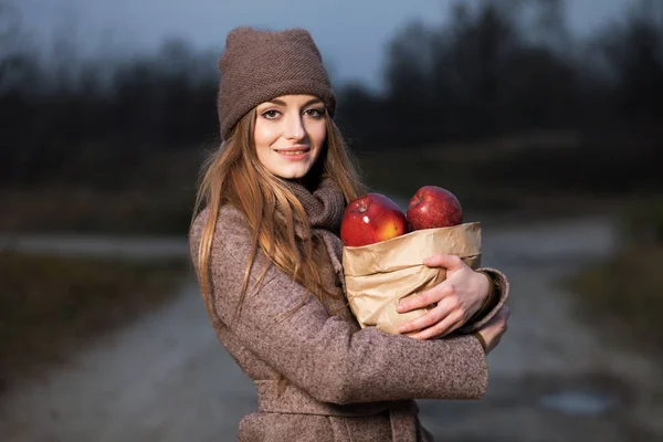 Chica en una gorra de punto y bufanda con una manzana en el otoño en la naturaleza . — Foto de Stock