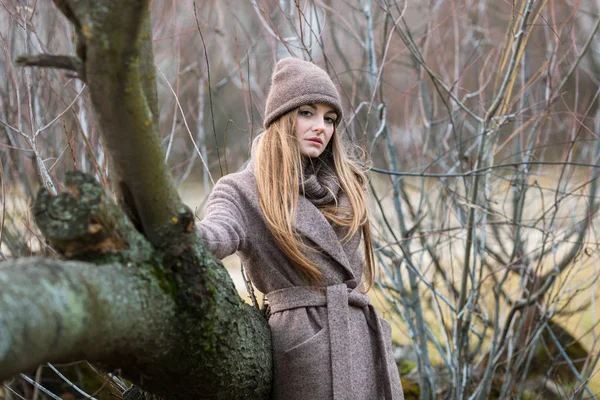 Meisje in een gebreide muts en sjaal in een omgevallen boom in de herfst op de natuur. — Stockfoto