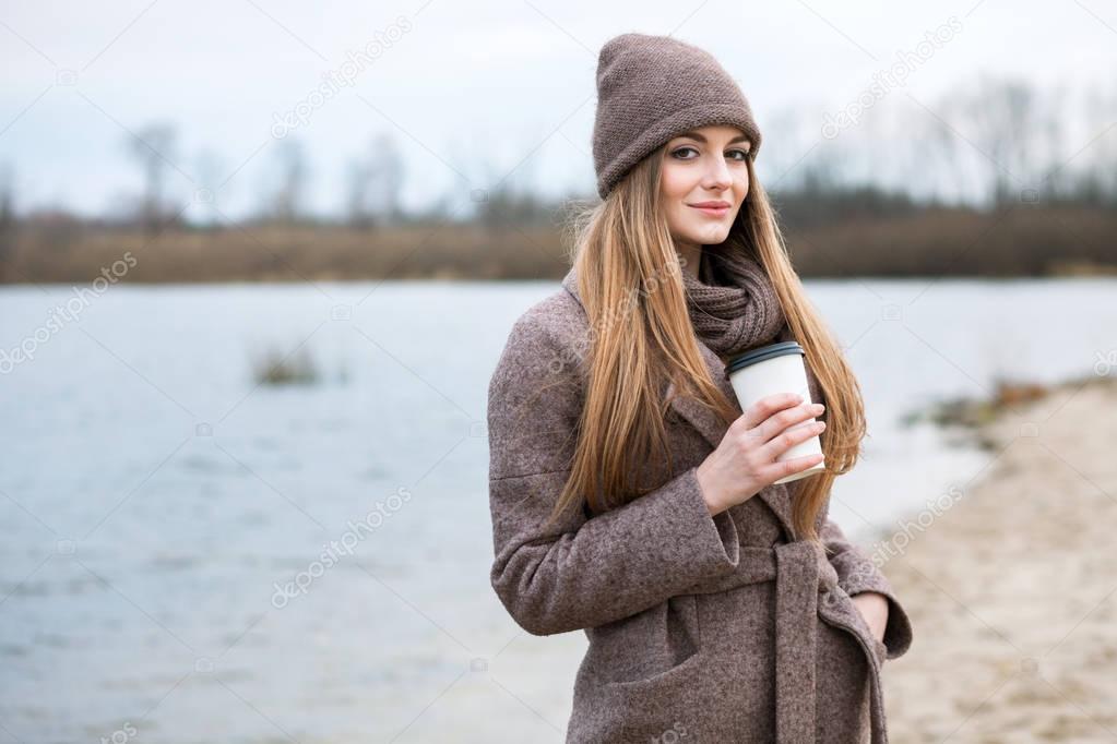 girl in a knitted hat and scarf with a mug in the fall on nature