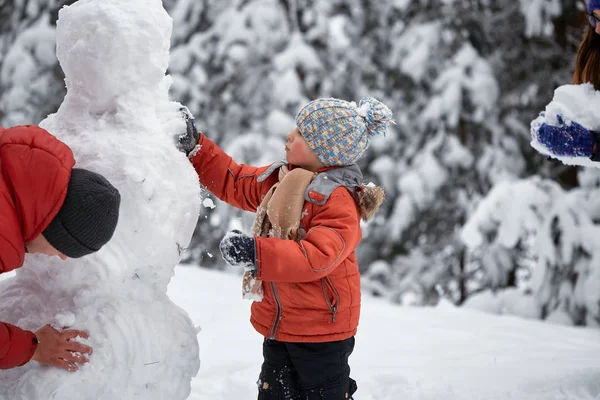 Diversión invernal. el niño esculpe el muñeco de nieve . — Foto de Stock