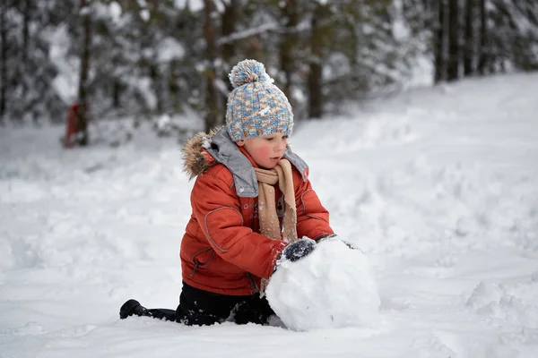 Diversión invernal. el niño esculpe el muñeco de nieve . — Foto de Stock