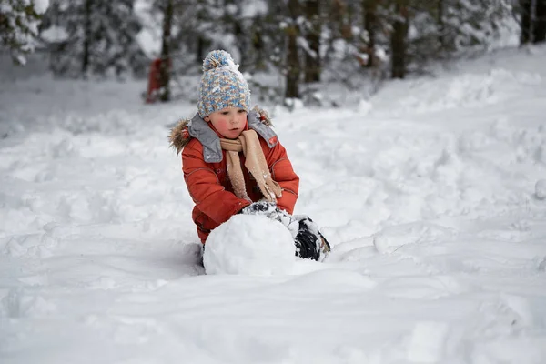 Diversión invernal. el niño esculpe el muñeco de nieve . — Foto de Stock