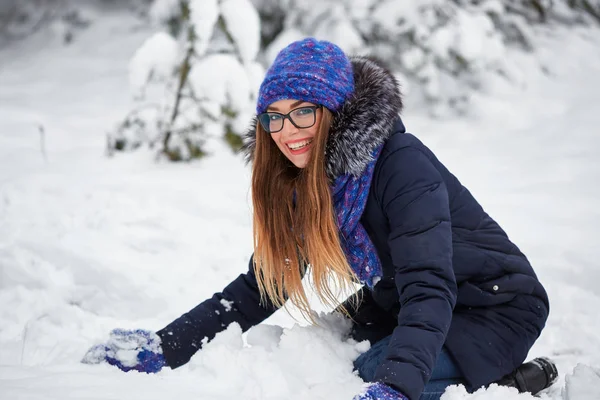 Diversão de inverno. menina em um chapéu de malha esculpe um boneco de neve . — Fotografia de Stock