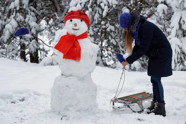 Winterspaß. Mädchen mit Strickmütze modelliert einen Schneemann. — Stockfoto