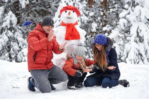 Diversión invernal. una chica, un hombre y un niño haciendo un muñeco de nieve . — Foto de Stock