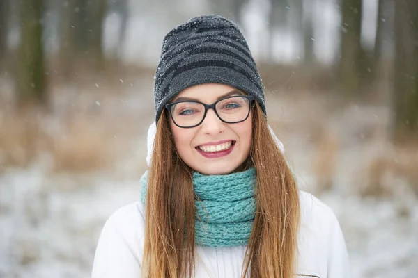 Portret van een vrolijk meisje met bril in een sneeuwval in de winter. — Stockfoto