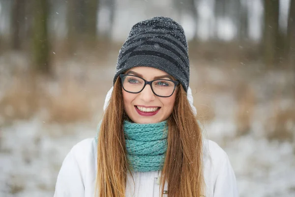 Retrato de uma menina alegre com óculos em uma queda de neve no inverno . — Fotografia de Stock