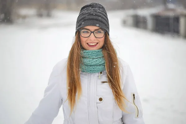 Retrato de uma menina alegre com óculos em uma queda de neve no inverno . — Fotografia de Stock
