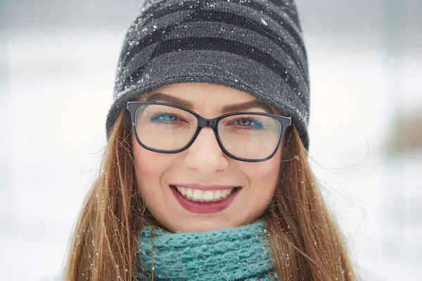 Portret van een vrolijk meisje met bril in een sneeuwval in de winter. — Stockfoto