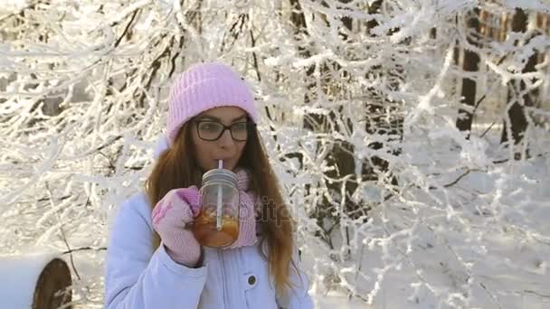 美丽的女孩在一个粉红色的帽子和手套在冬天的雪森林喝茶 — 图库视频影像