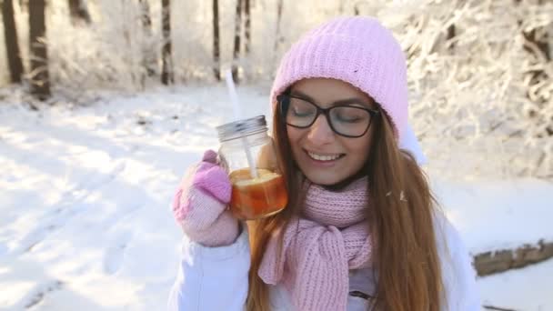 美丽的女孩在一个粉红色的帽子和手套在冬天的雪森林喝茶 — 图库视频影像