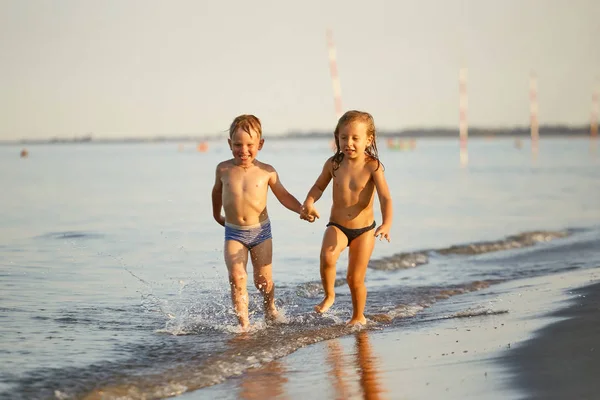 Menina e menino estão correndo ao longo da costa do mar — Fotografia de Stock