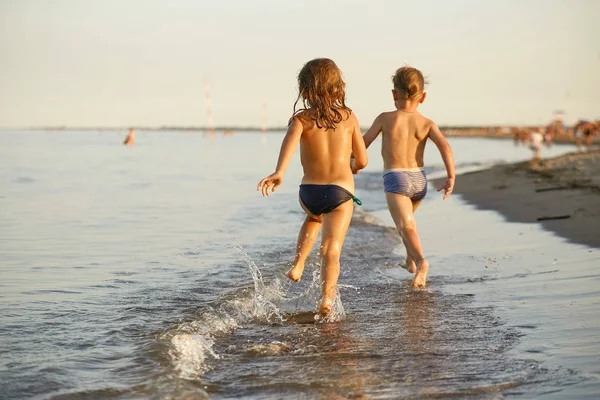 Menina e menino estão correndo ao longo da costa do mar — Fotografia de Stock