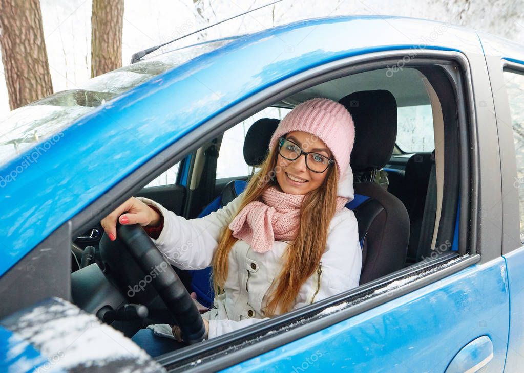 girl in a pink hat driving a blue car in winter.