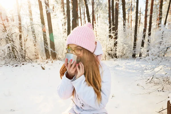 Κορίτσι σε ένα ροζ καπέλο που πίνει τσάι από ένα θερμός το χειμώνα στο δάσος. — Φωτογραφία Αρχείου