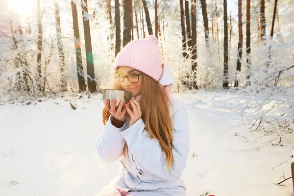 Girl in a pink hat drinking tea from a thermos in the winter in the forest. — Stock Photo, Image