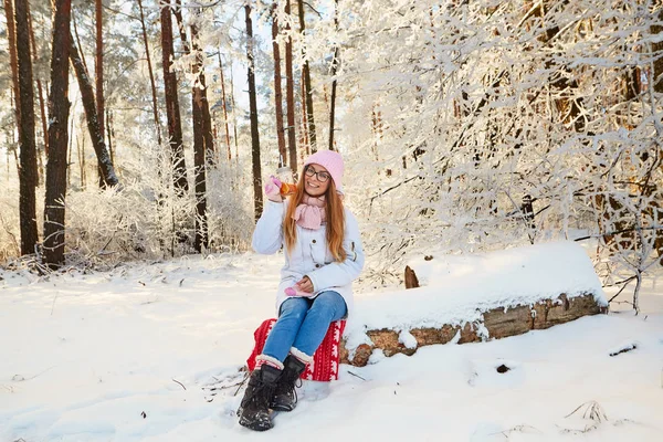 Menina em um chapéu rosa bebendo vinho quente no inverno na floresta . — Fotografia de Stock