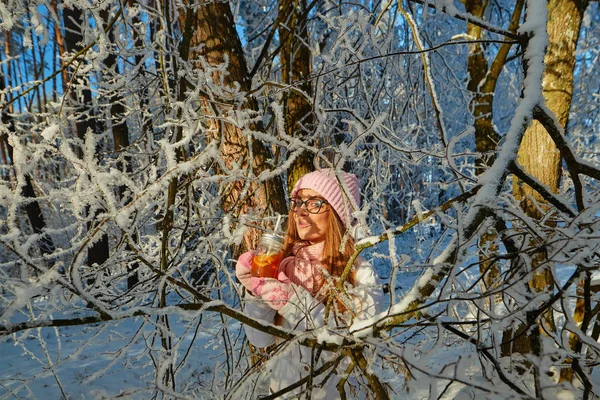 Menina em um chapéu rosa bebendo vinho quente no inverno na floresta . — Fotografia de Stock