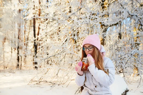 Menina em um chapéu rosa bebendo vinho quente no inverno na floresta . — Fotografia de Stock