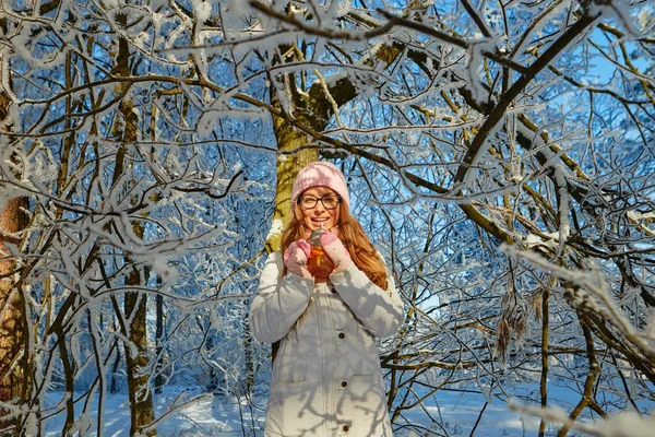 Menina em um chapéu rosa bebendo vinho quente no inverno na floresta . — Fotografia de Stock