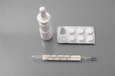 gri bir arka plan stüdyo burnuna tabletler ve bir sprey ile tıbbi termometre.