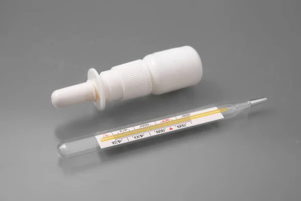 Medizinisches Thermometer mit Tabletten und Nasenspray auf grauem Hintergrund im Studio. — Stockfoto