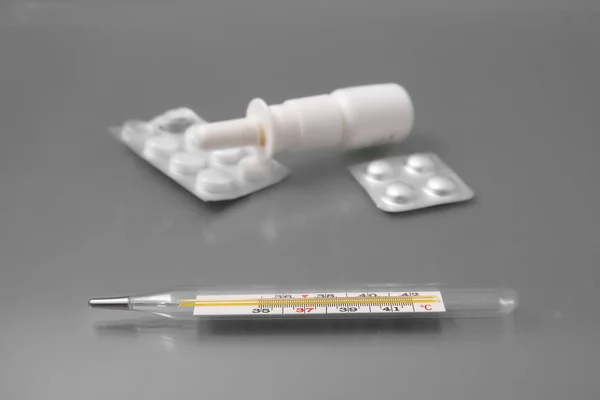 Termometr medyczny z tabletek i spray do nosa na szarym tle w studio. — Zdjęcie stockowe